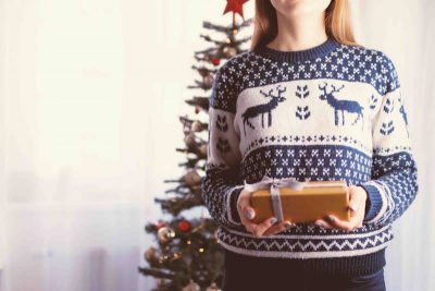 woman wearing a Christmas pullover holding a gift